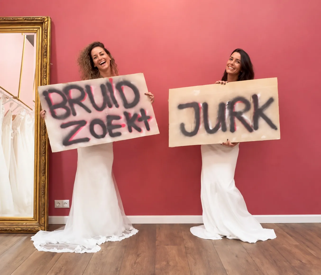 Twee bruiden houden de borden BRUID ZOEKT en JURK omhoog