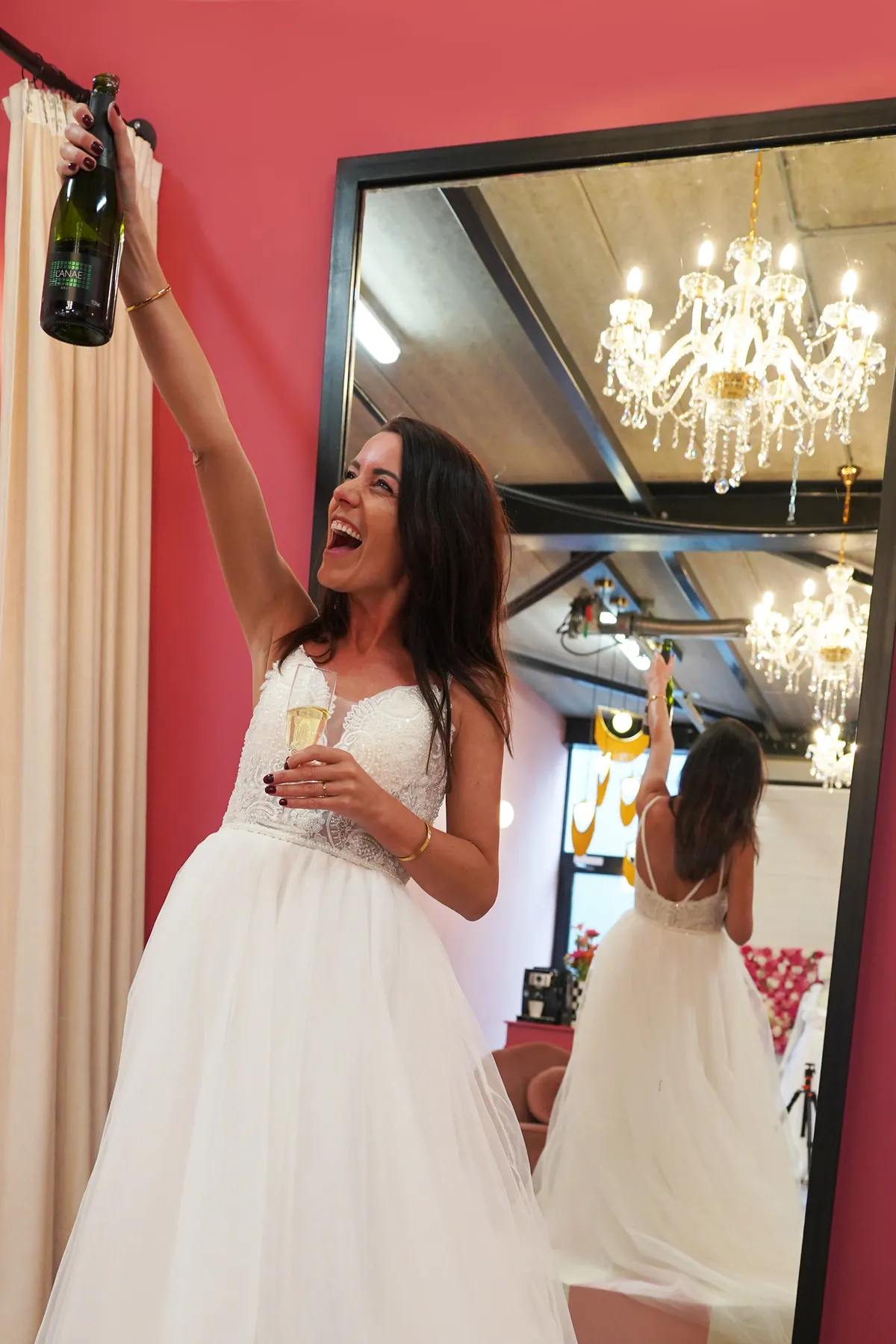 Bruid heft een fles champagne voor de spiegel